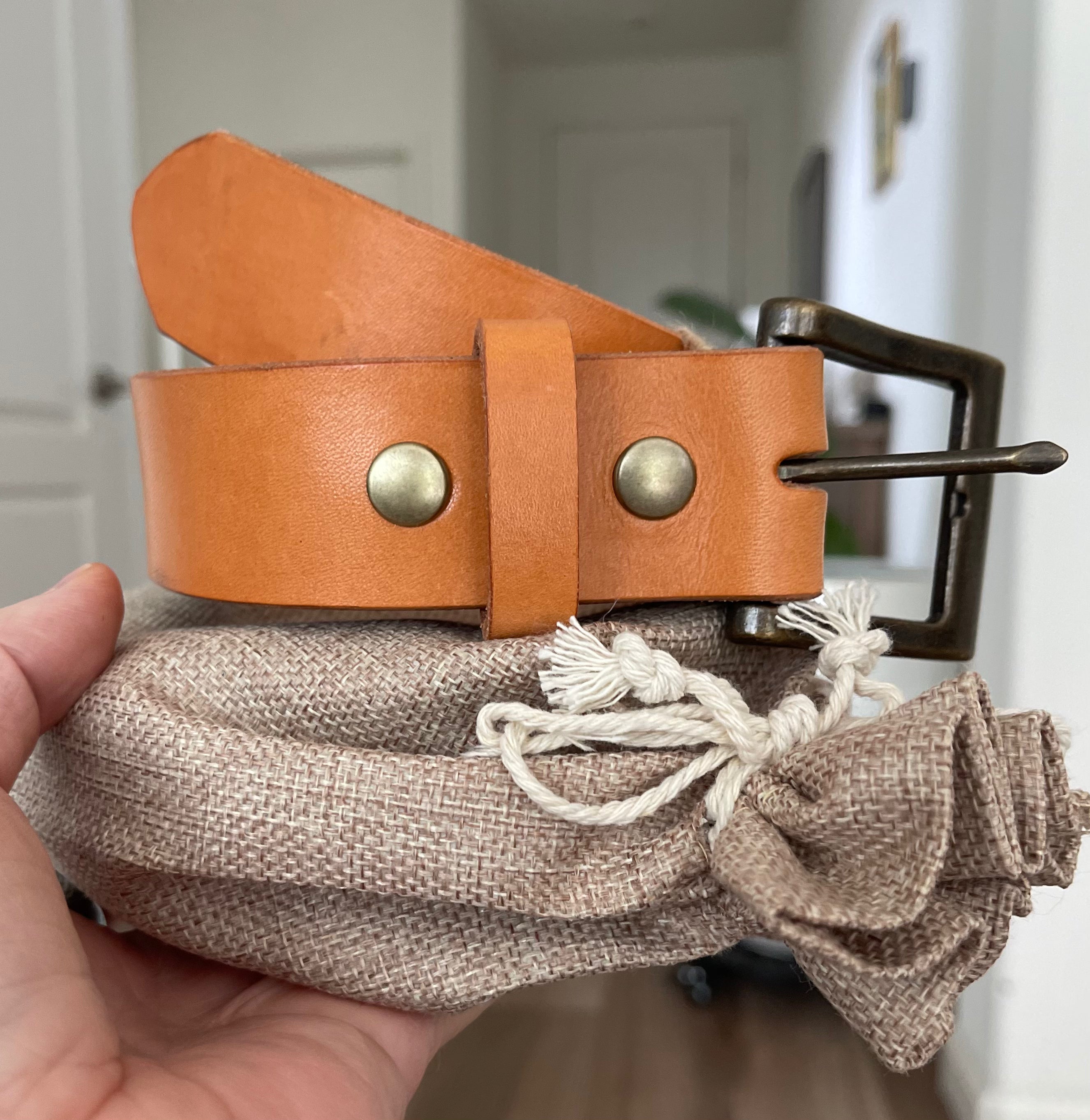 London Tan Hermann Oak English Bridle belt with antique brass buckle held over its canvas pouch