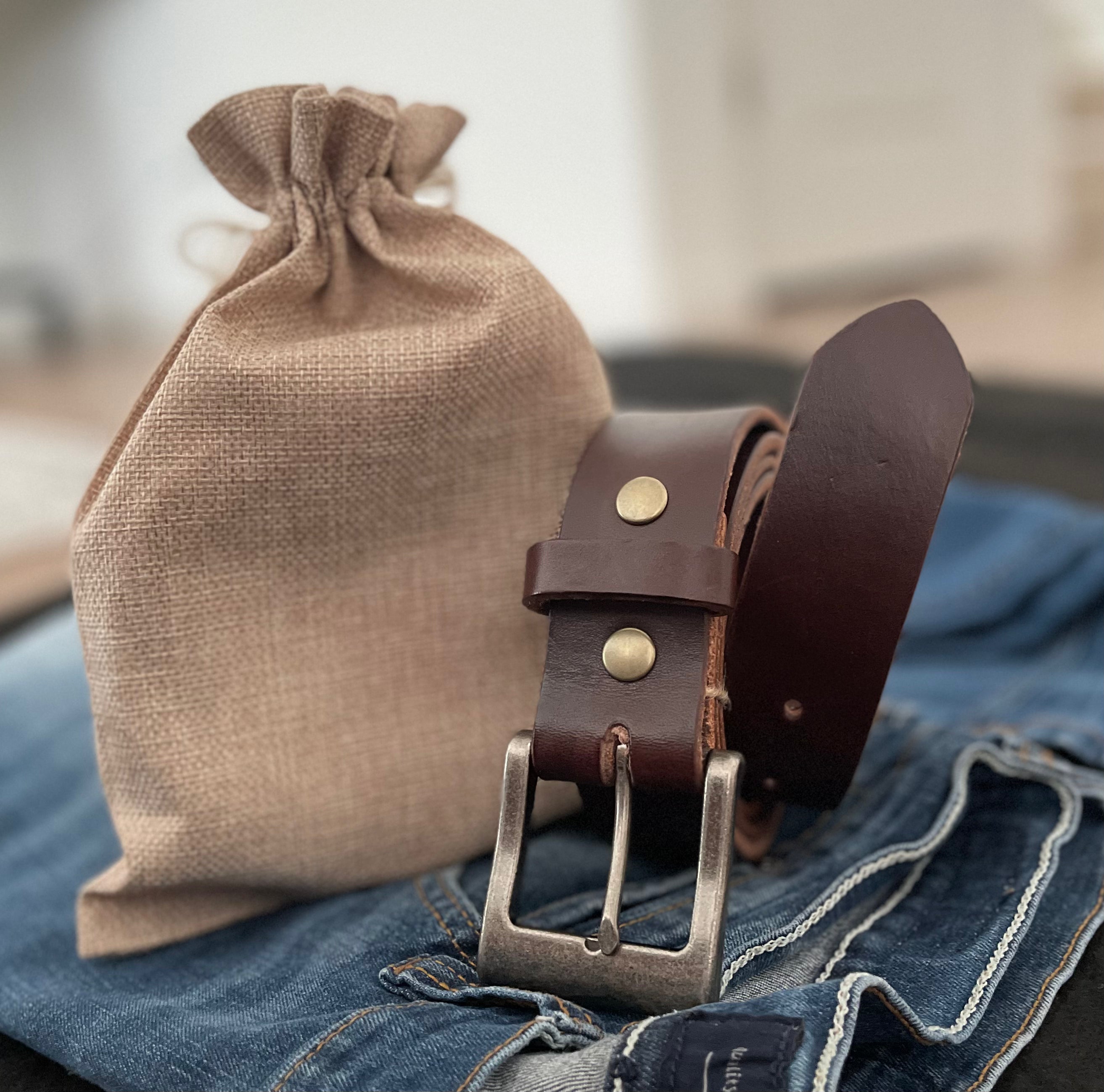 Havana Brown Hermann Oak English Bridle belt with antique nickel buckle and its canvas drawstring pouch on denim