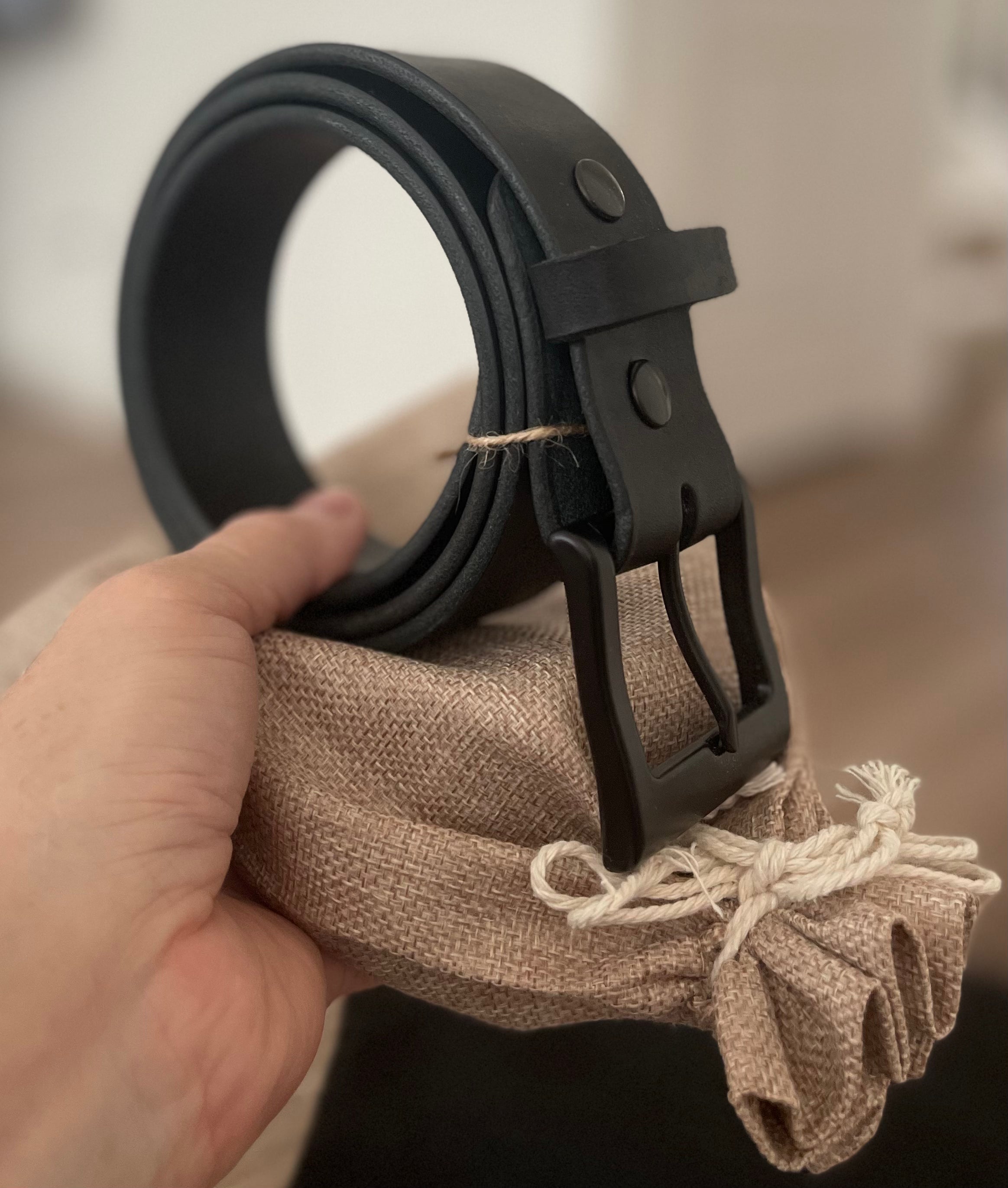 Black Hermann Oak English Bridle belt with matte black buckle held over its canvas pouch